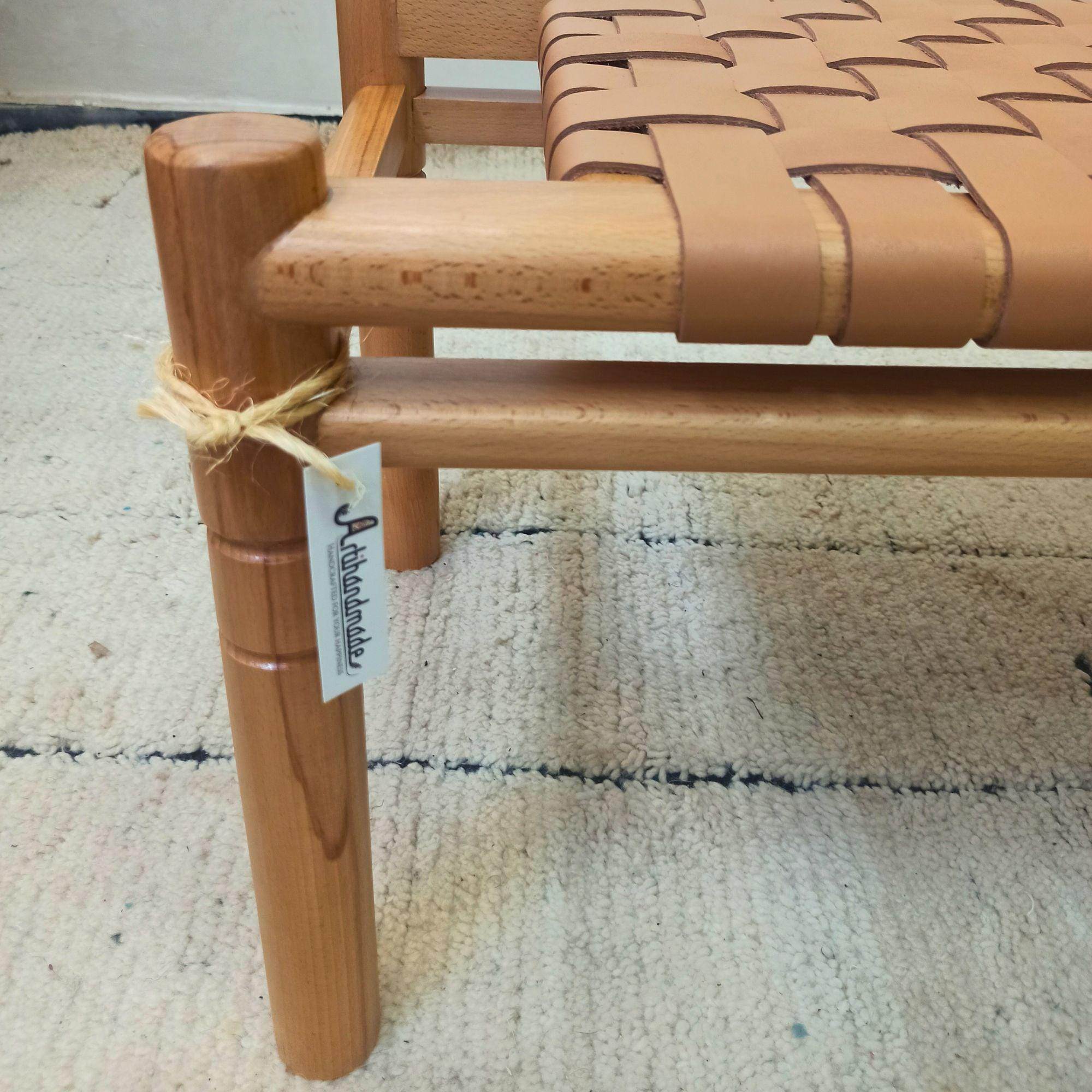 Wooden bench with woven leather seat on a textured surface, featuring a brand tag Artihandmade.