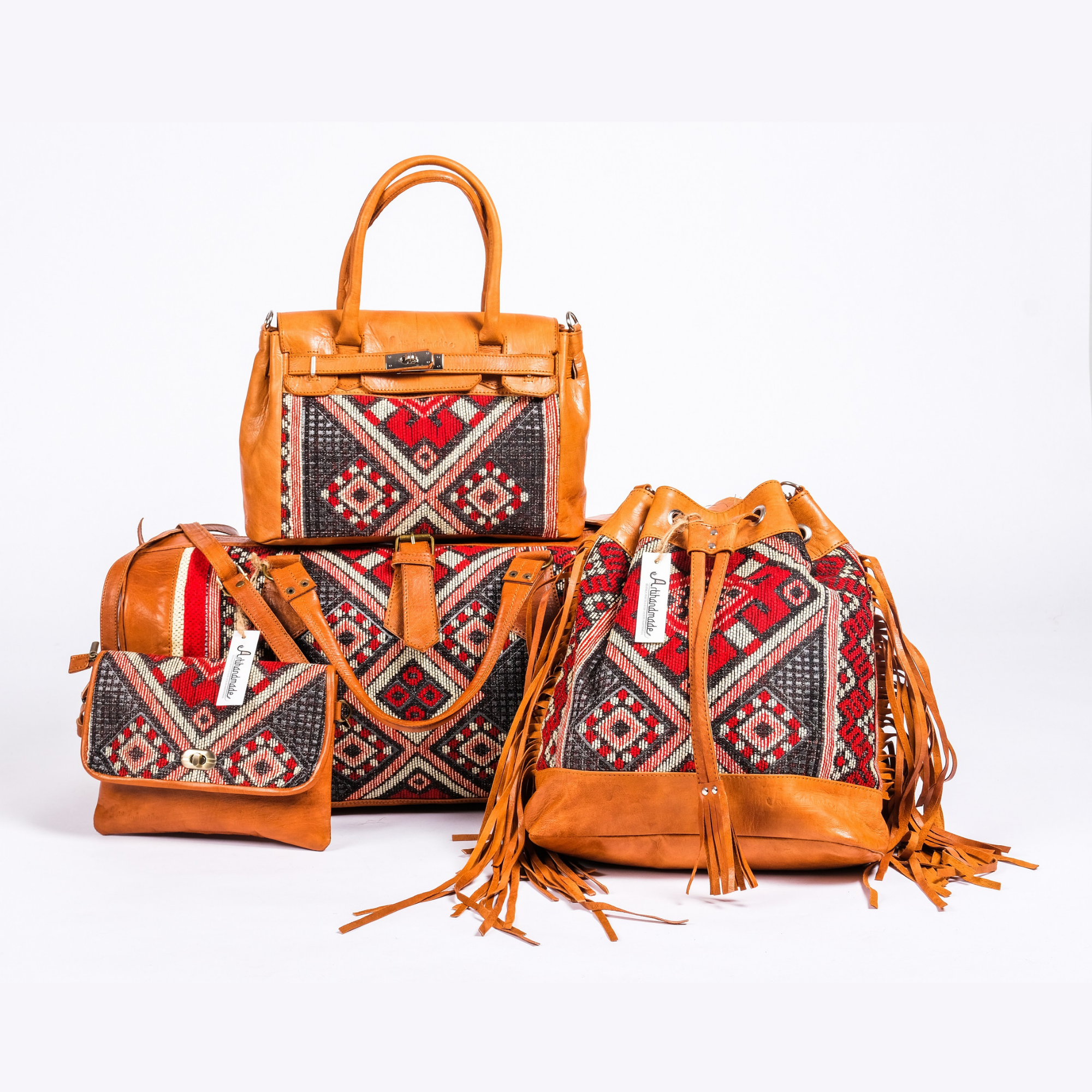 A set of four leather handbags with geometric kilim patterns, including a small shoulder bag, a medium tote bag, a larger carry-on bag, and a solid brown leather bag, all with fringed accents.