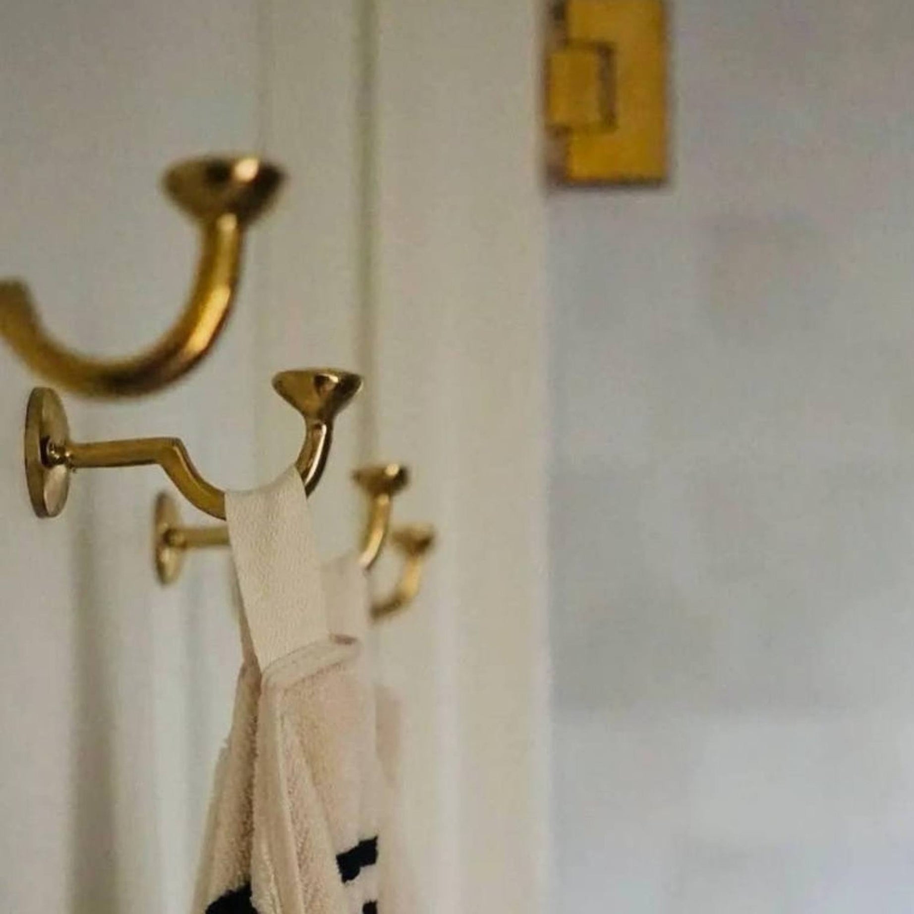 Gold hooks on a white door with a beige garment hanging from one of them.