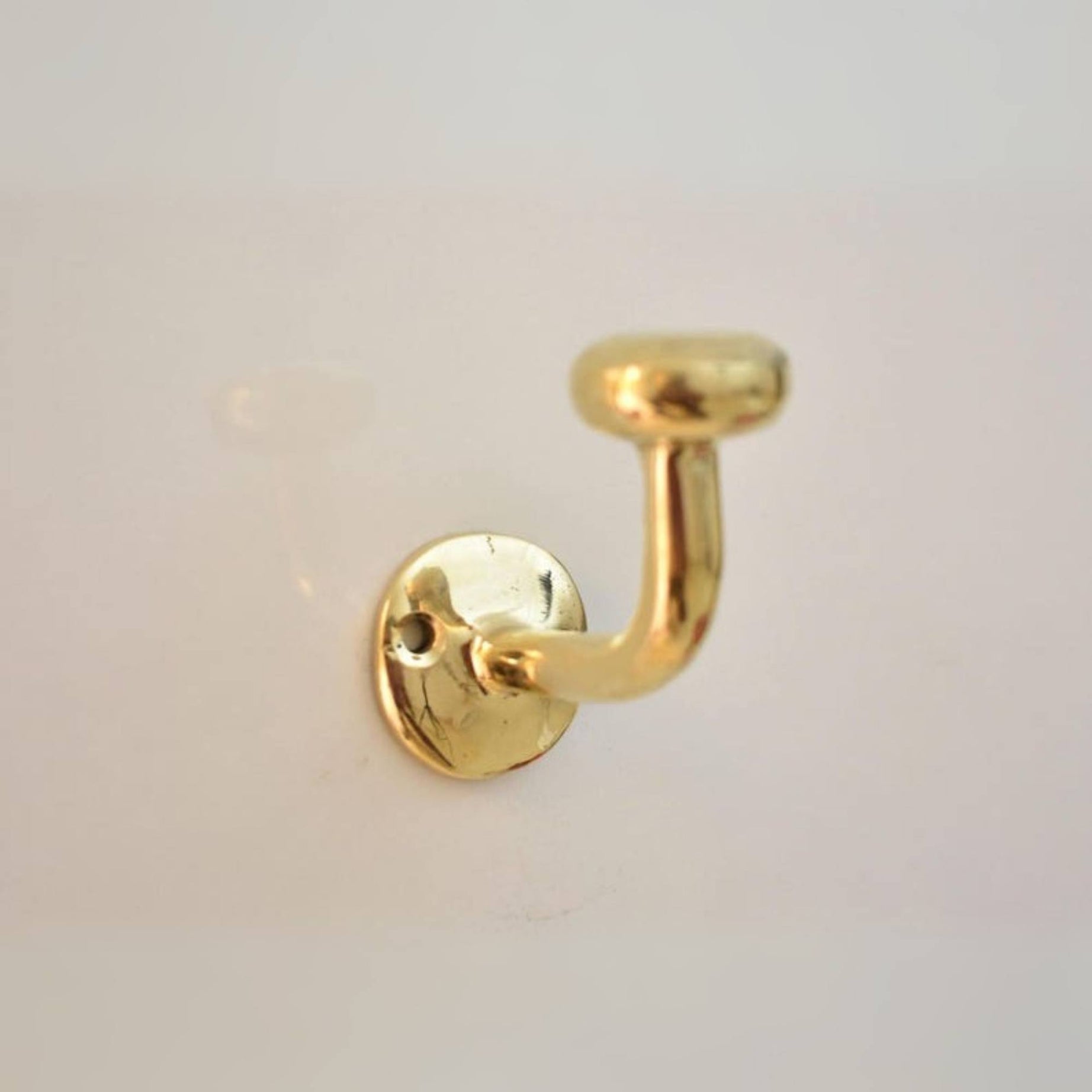 Gold brass wall hook on a light gray background