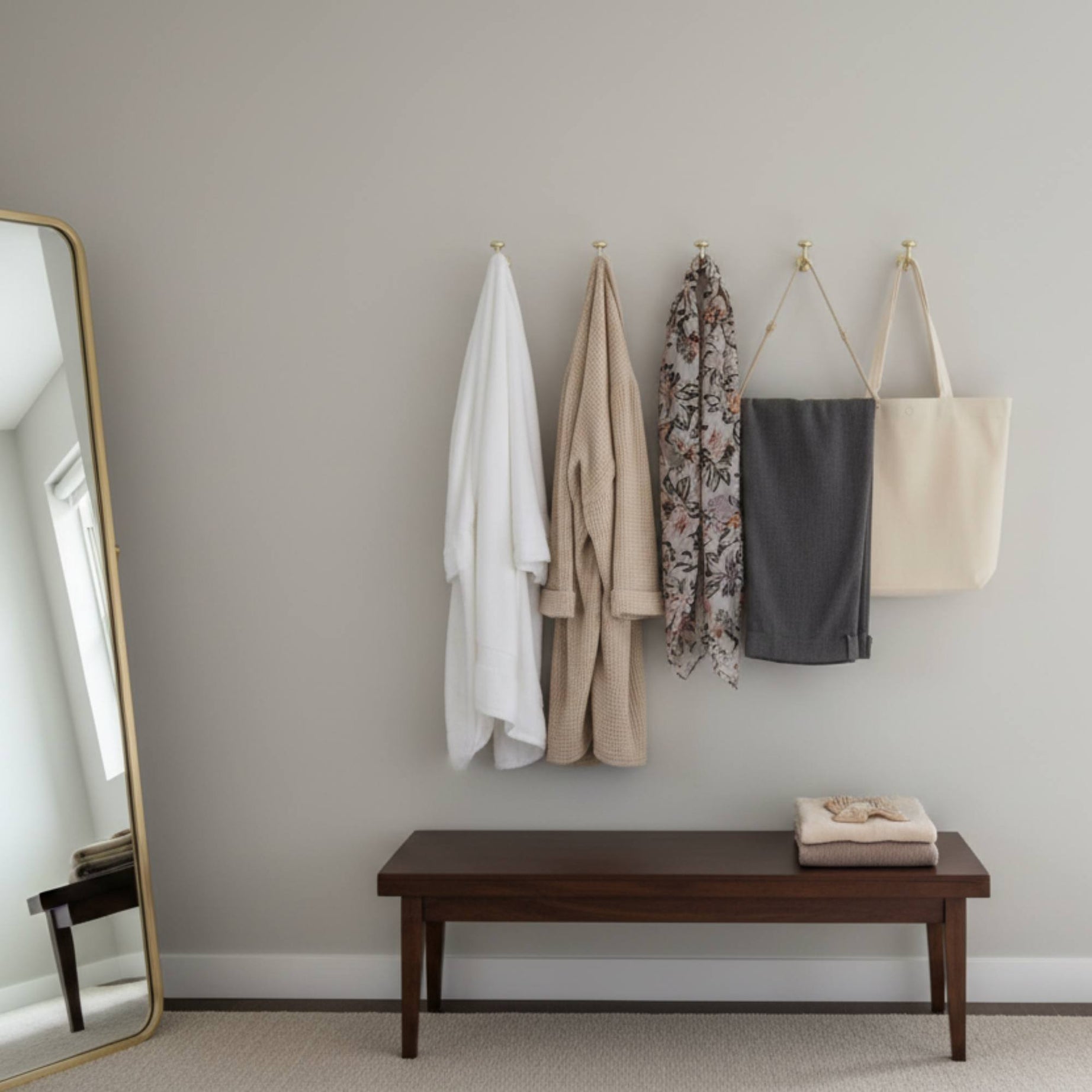 Hanging clothes and a bench in a room with a large mirror.