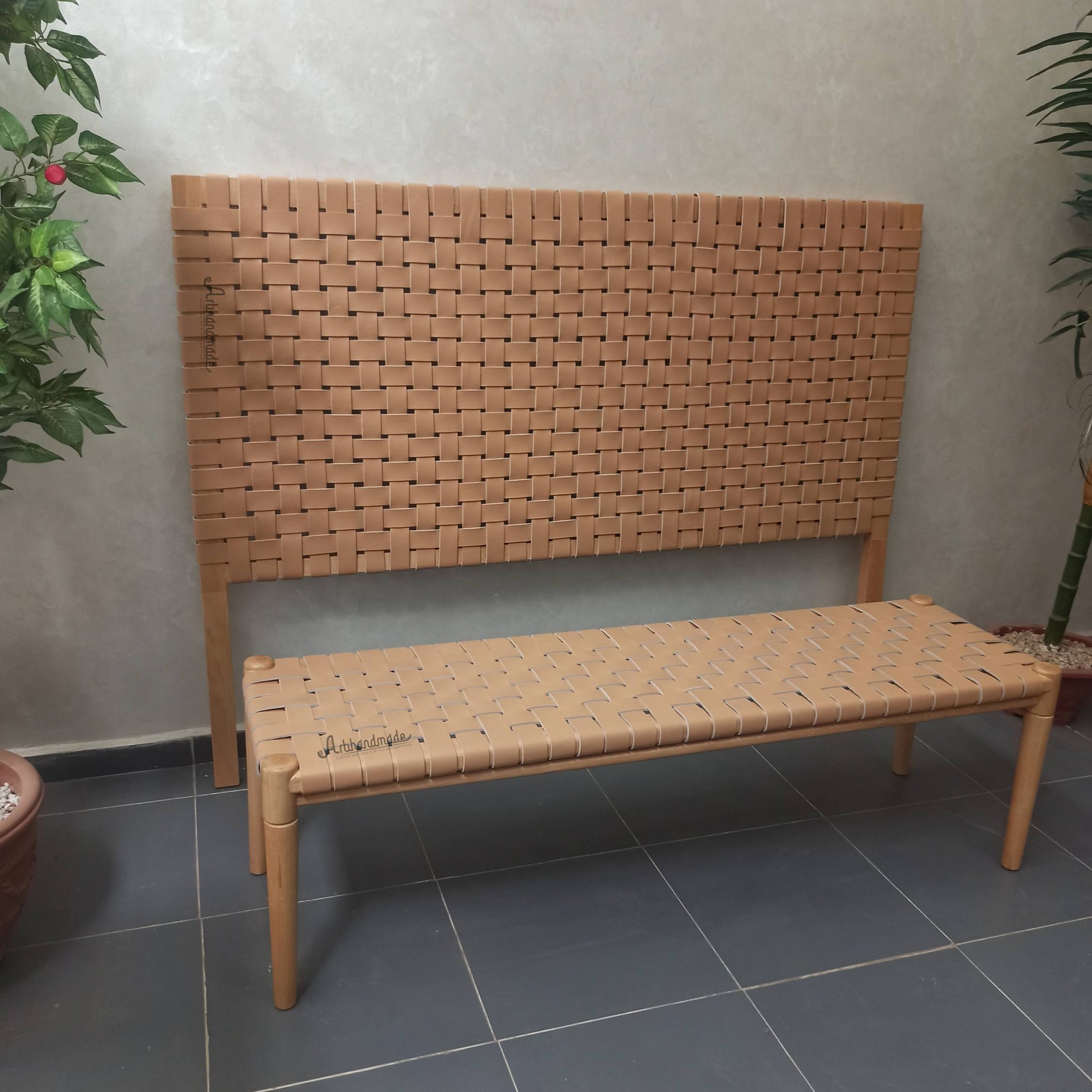 Woven bench against a plain wall with plants on either side.