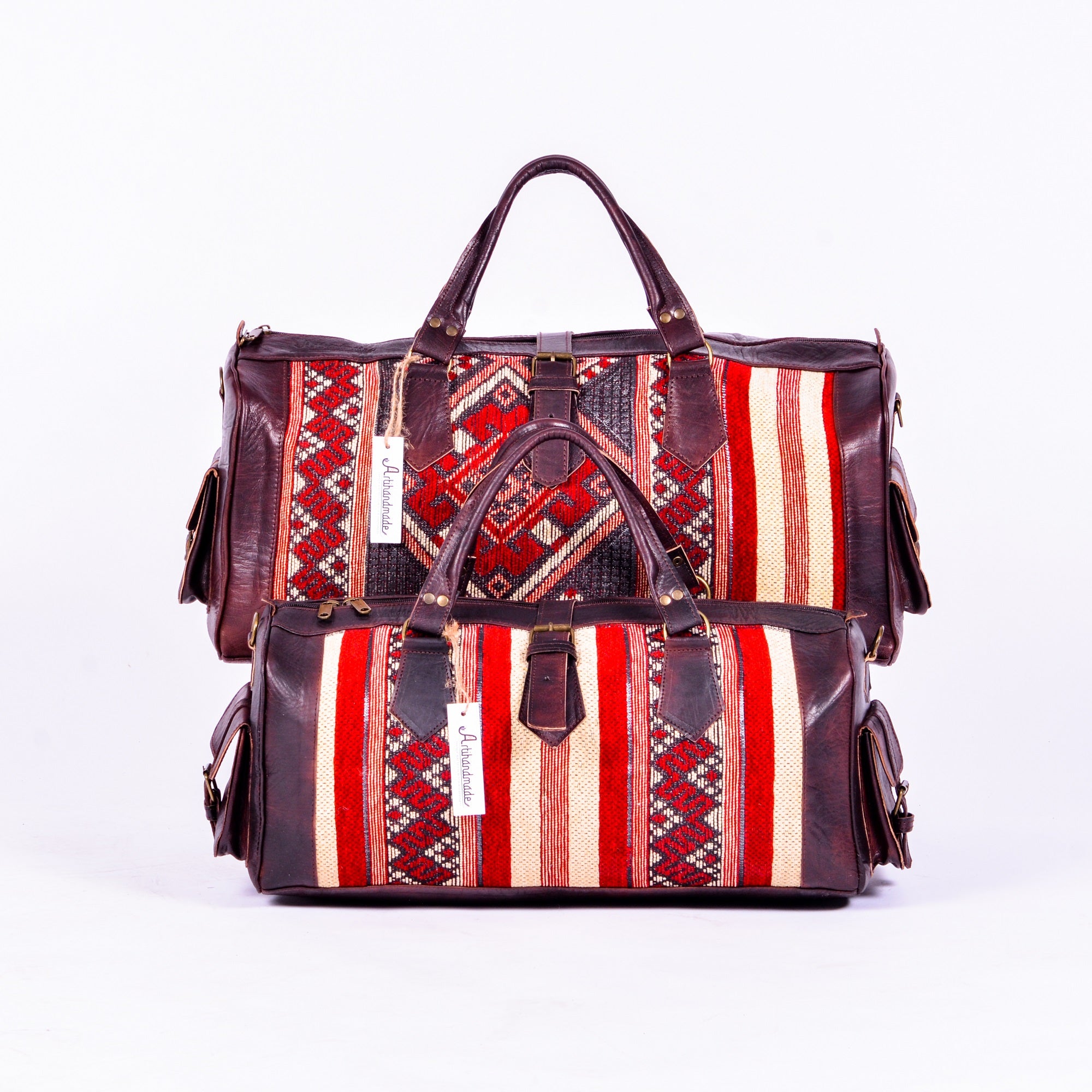 Two duffel bags with a combination of leather and kilim designs, featuring a striped pattern in red, brown, and beige colors, with a leather finish and metal hardware.